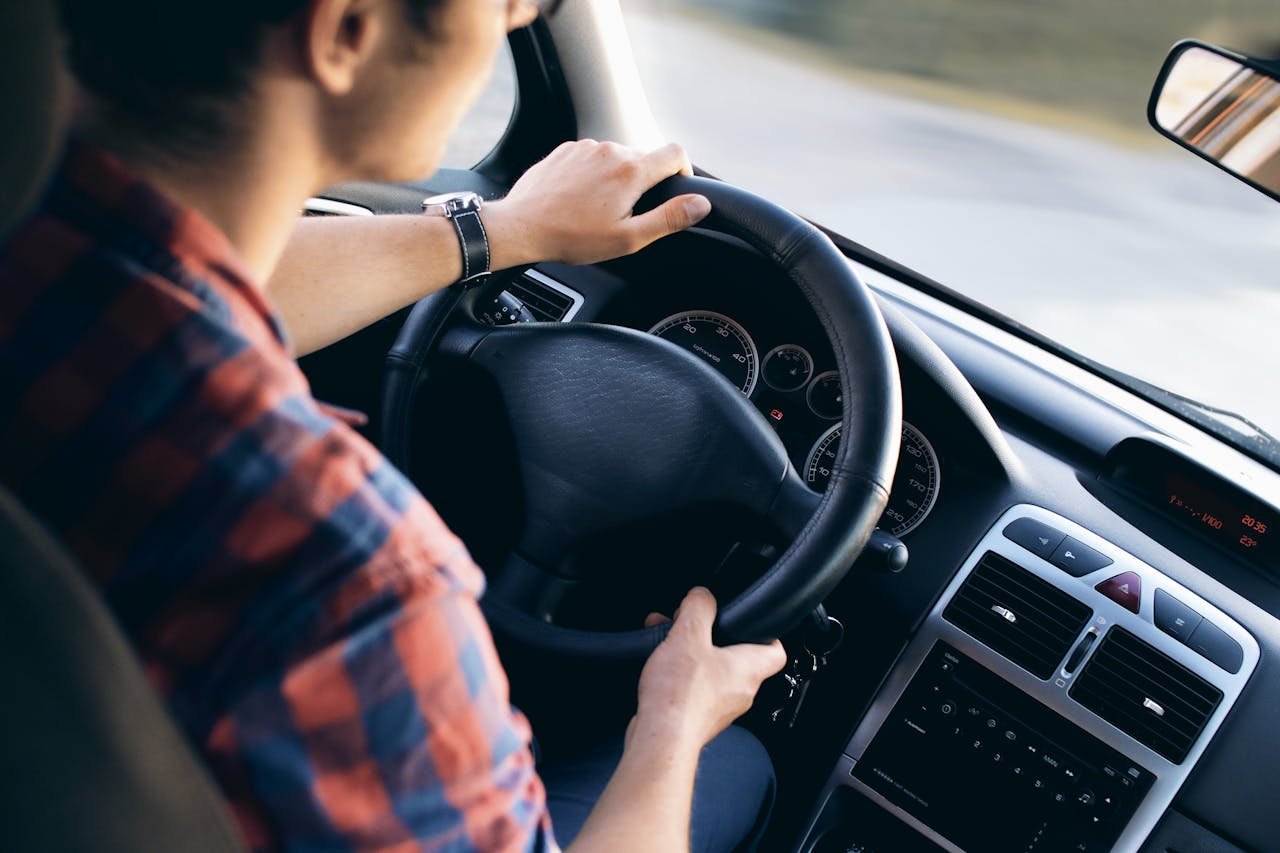 why-choose-us Close-up view of a man driving a modern car, showing dashboard and steering details.